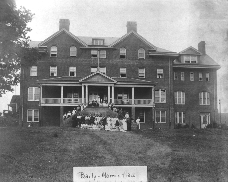 Black and white photograph of Baily-Morris Hall, a building on the campus of Christiansburg Industrial Institute. Several African American teachers stand on a staircase in front of the building.