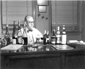 Man with liquor bottles on a desk and animated birds overheard.